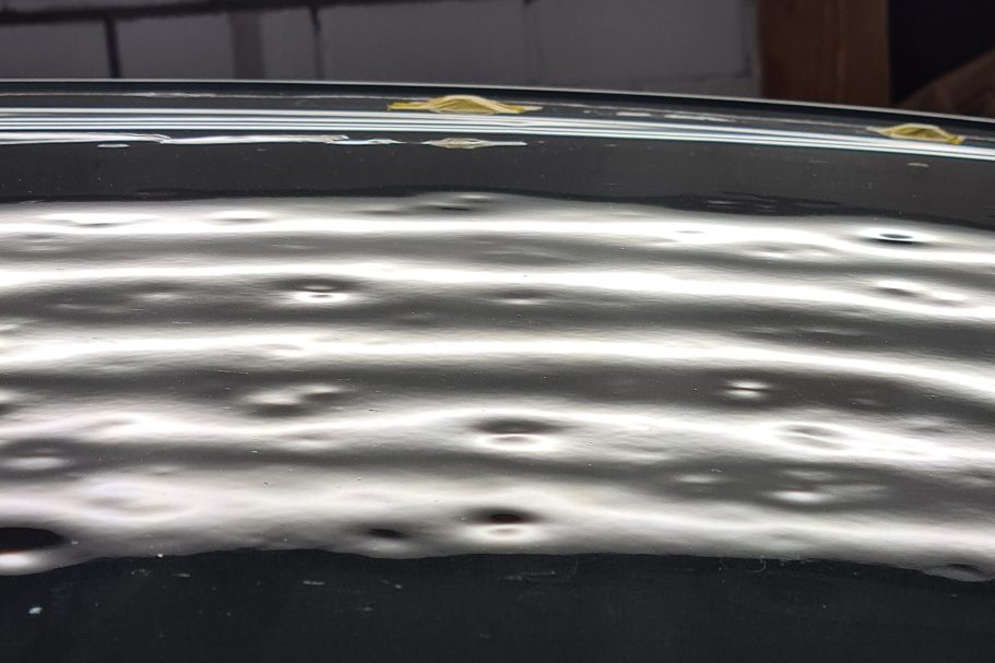 Autodach mit Hagelschaden Große Hagel Dellen auf dem Autodach, sichtbar mit der LED-Streifenlampe, Oberfläche wellenförmige Reflektionen und glänzender Textur.